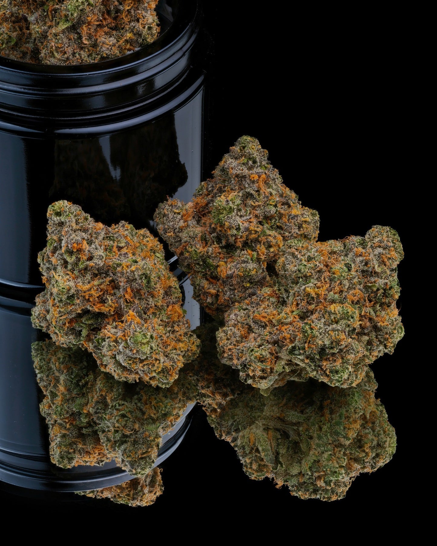 Close-up of cannabis buds with a black container on a reflective surface