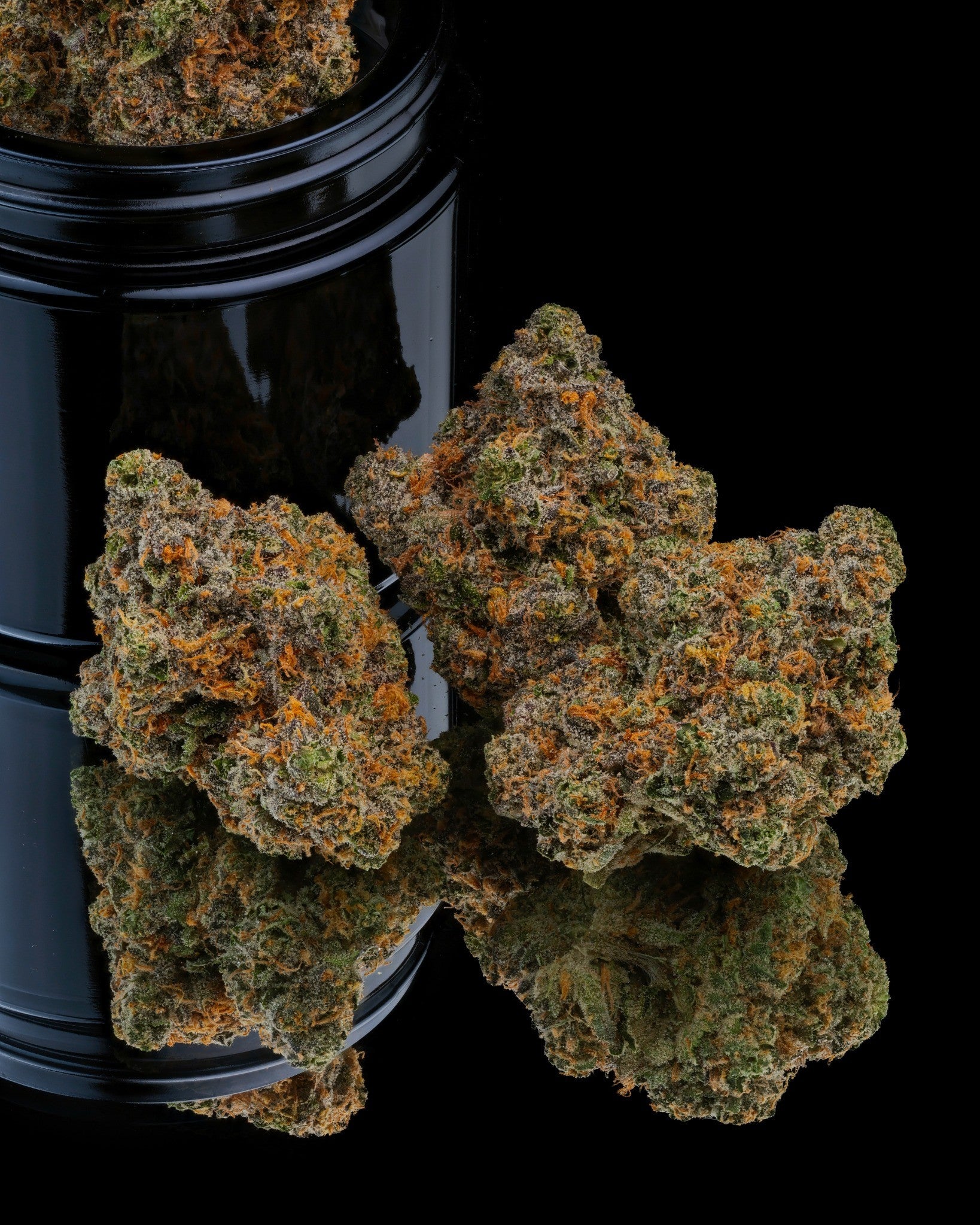 Close-up of cannabis buds with a black container on a reflective surface