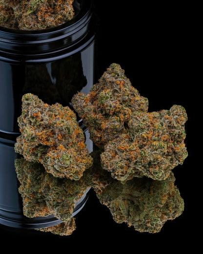 Close-up of cannabis buds with a black container on a reflective surface